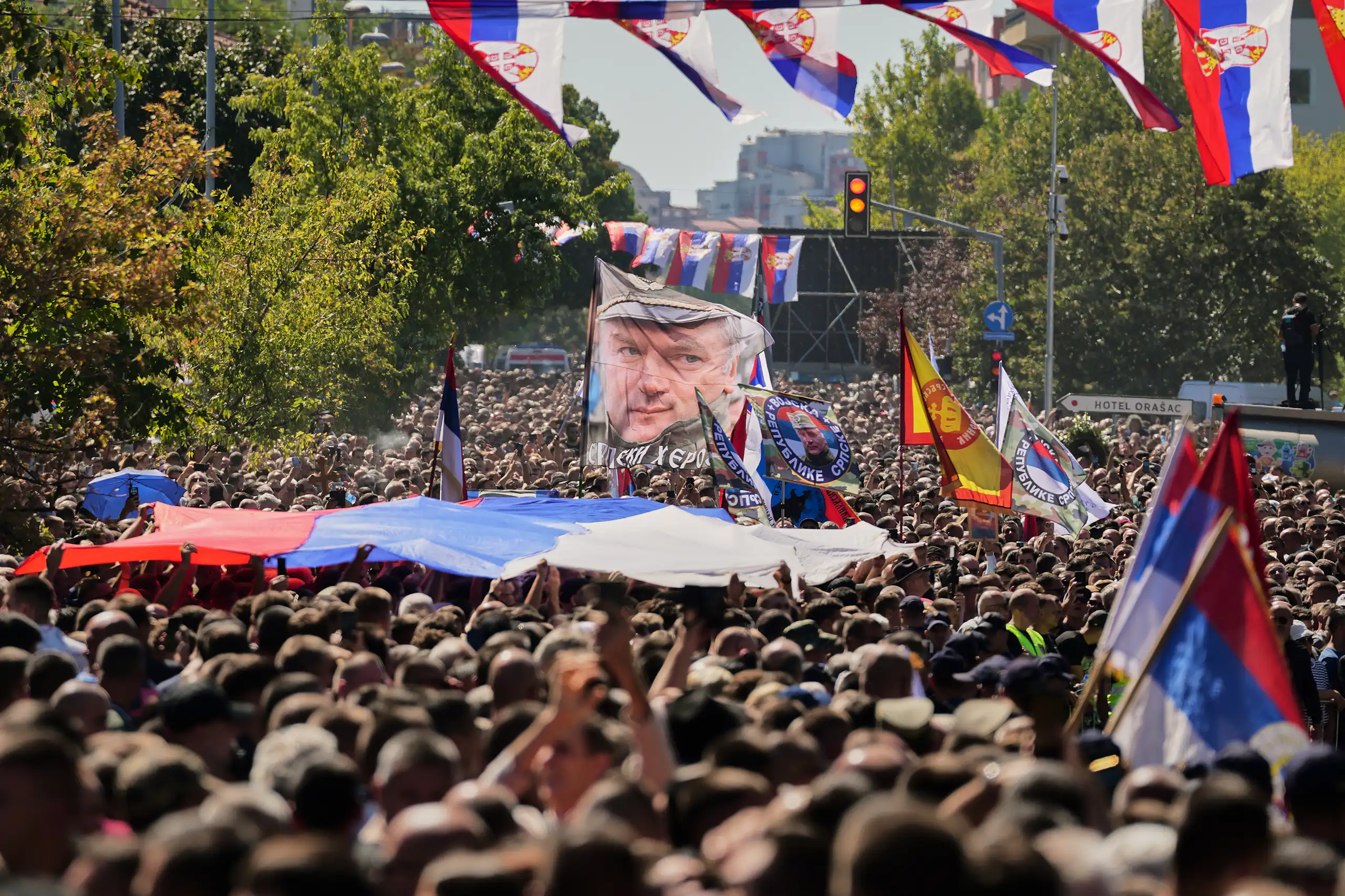 A crowd of people carrying flags depicting Ratko Mladić face and the Serbian flag