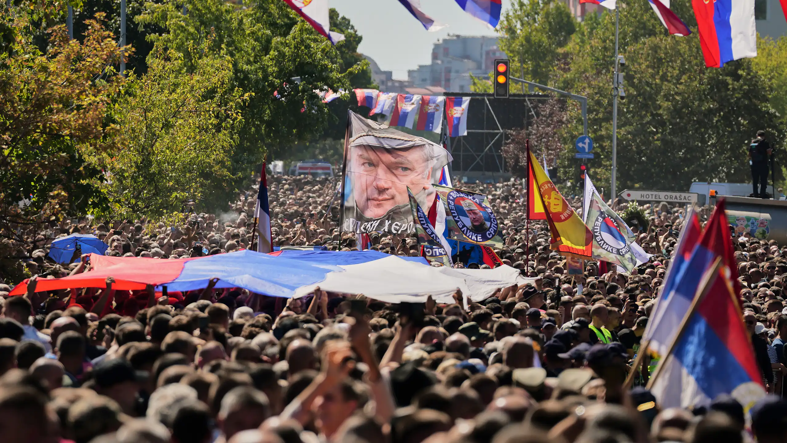 A crowd of people carrying flags depicting Ratko Mladić face and the Serbian flag