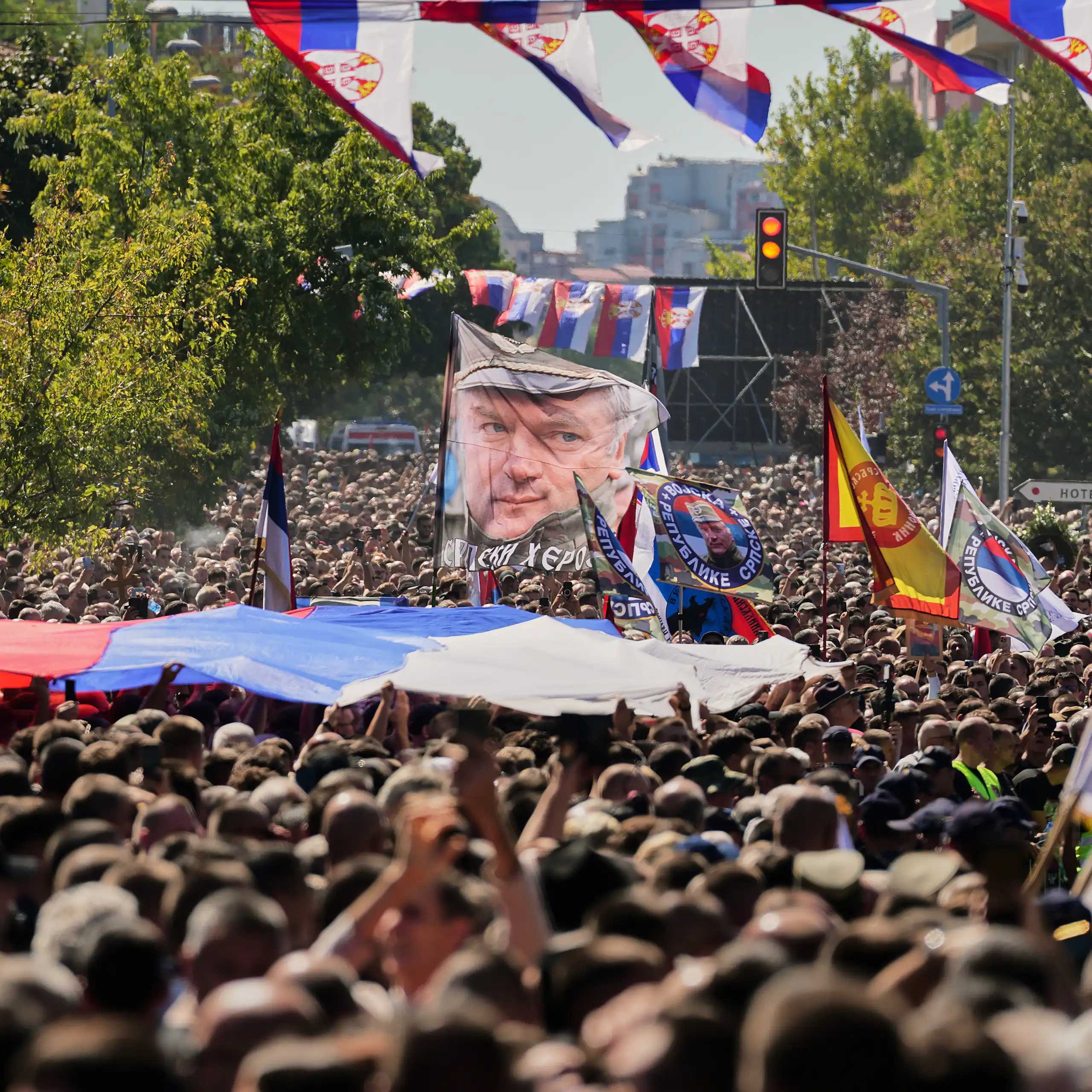 A crowd of people carrying flags depicting Ratko Mladić face and the Serbian flag