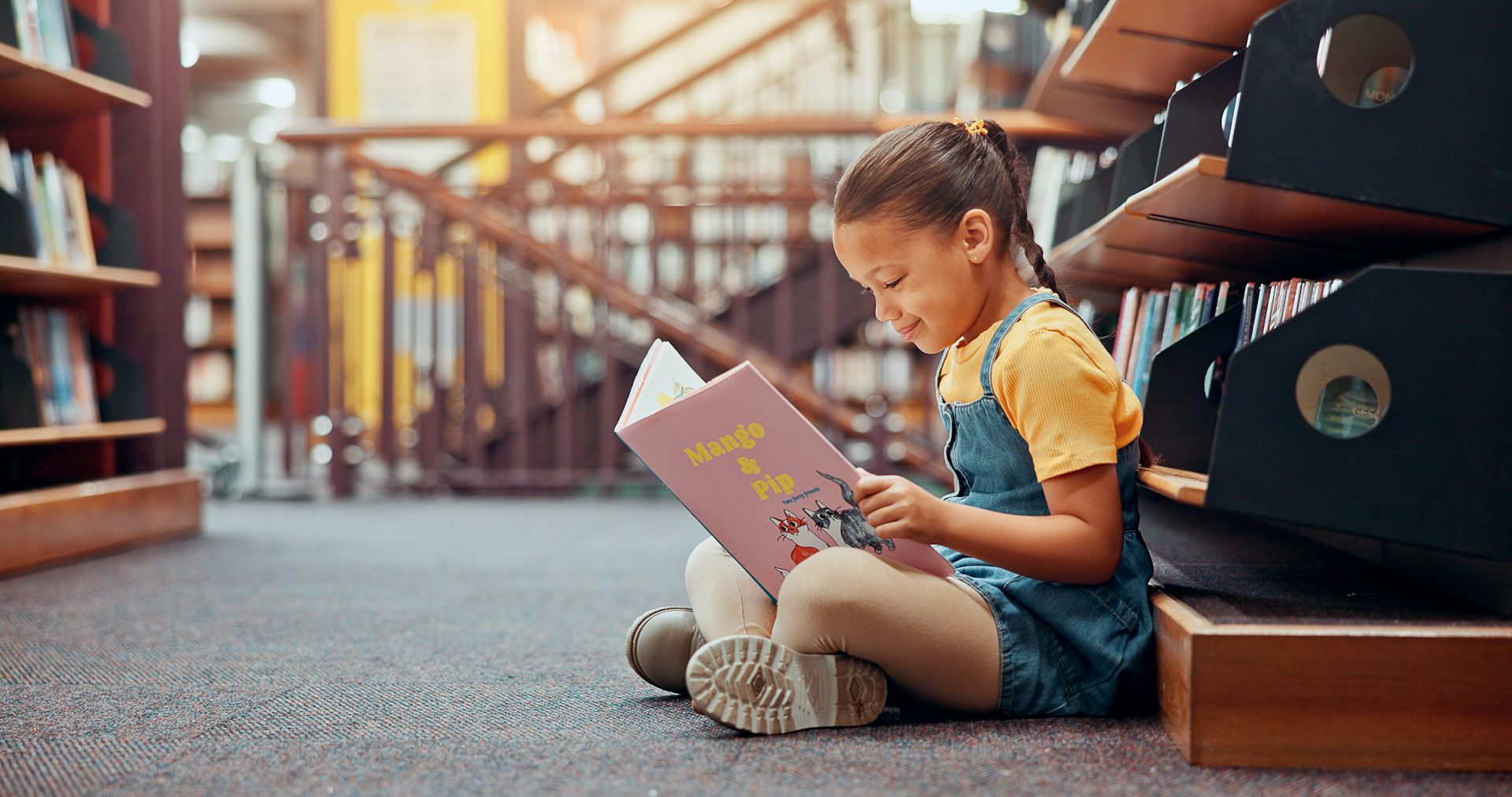 Una nena llig un llibre asseguda a terra.