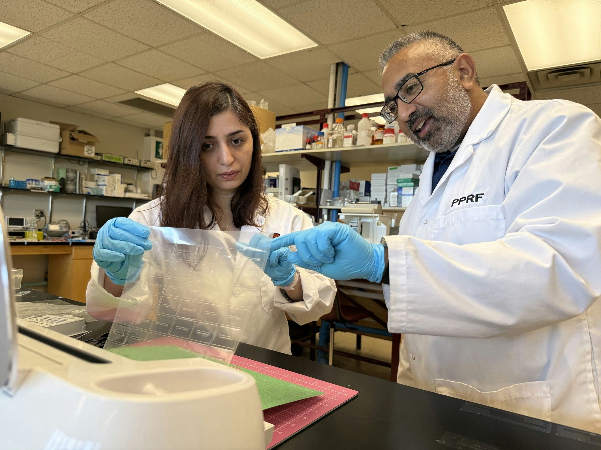 Une femme et un homme en blouse de laboratoire examinent un appareil technologique