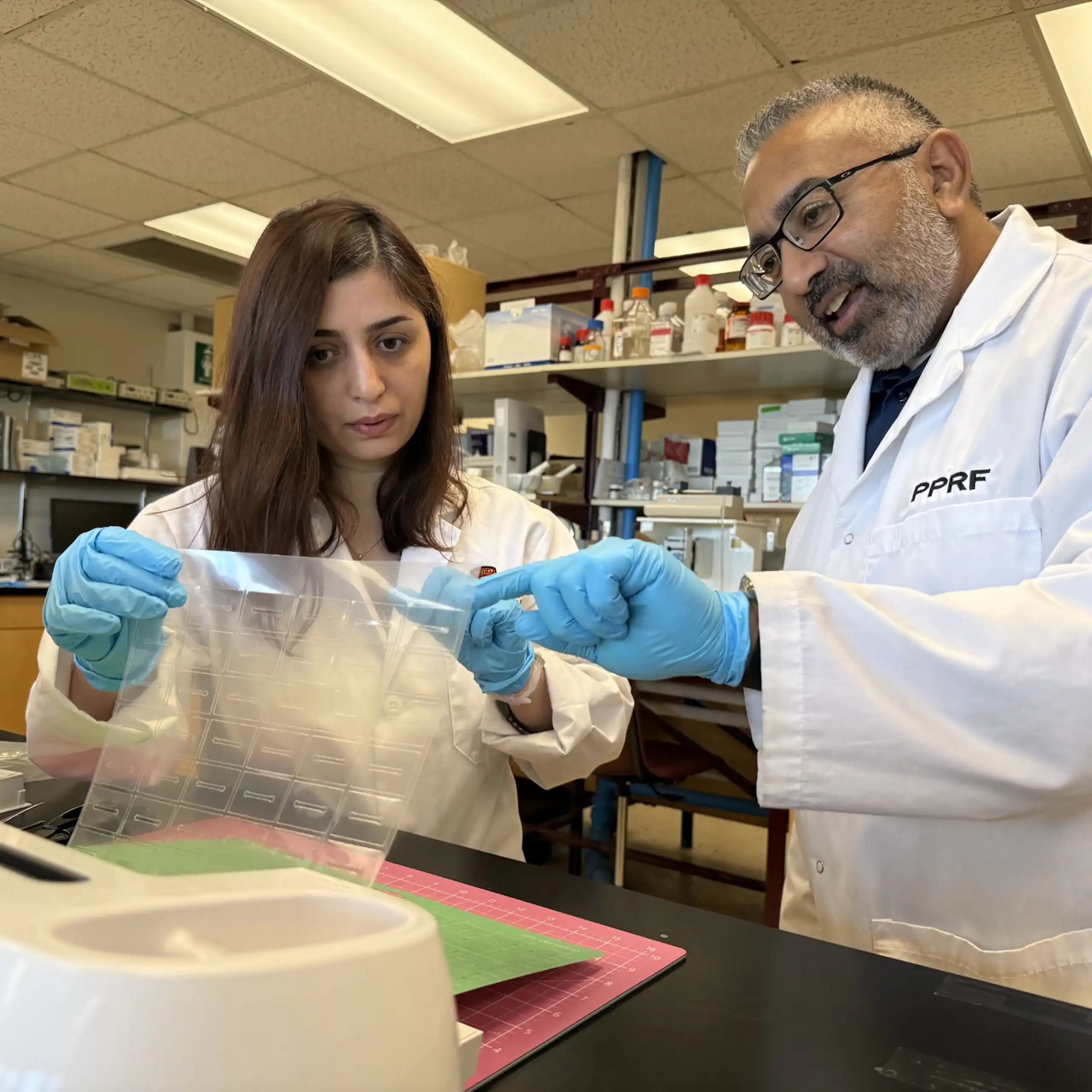 Une femme et un homme en blouse de laboratoire examinent un appareil technologique