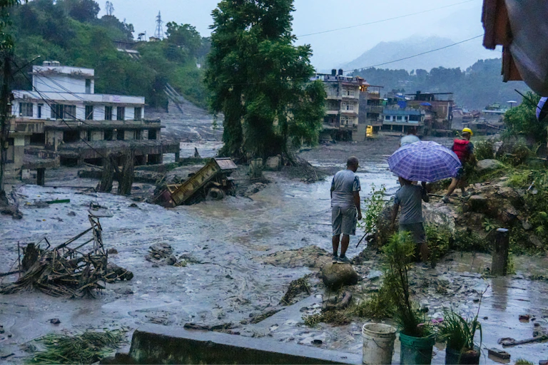 A few people stand at the side of a large area of water caused by the massive flooding in Nepal.