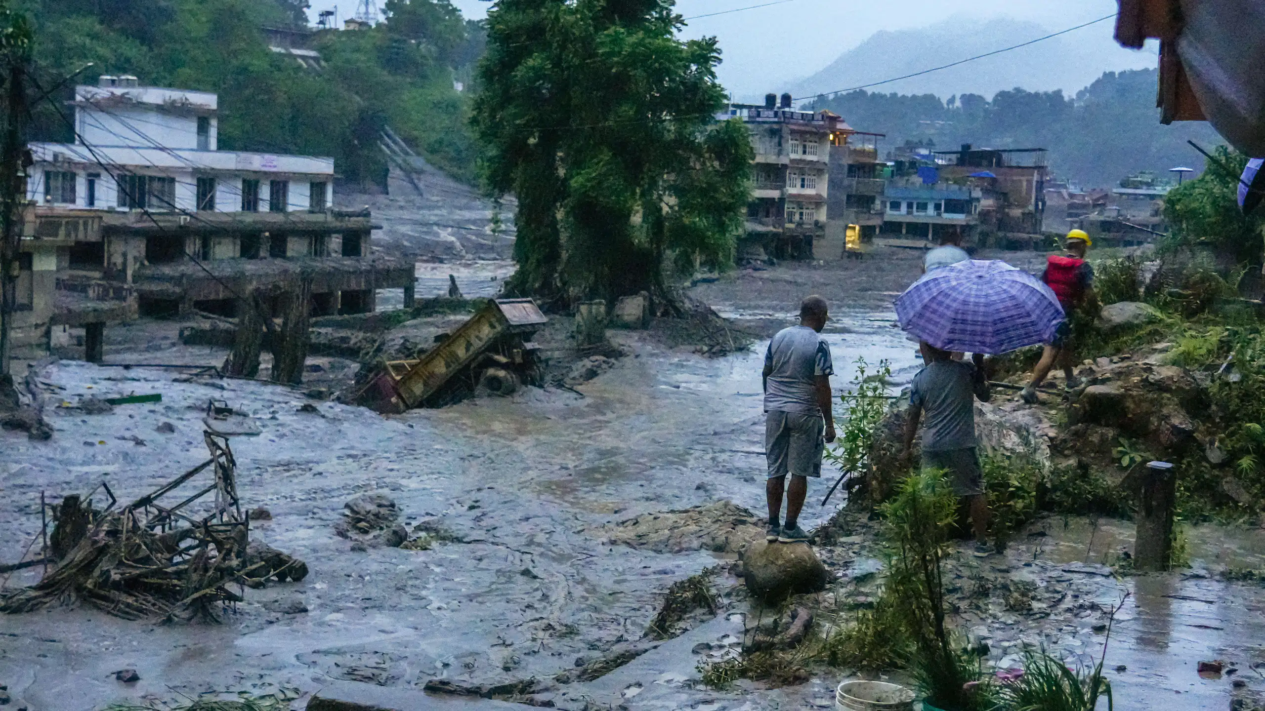 A few people stand at the side of a large area of water caused by the massive flooding in Nepal.