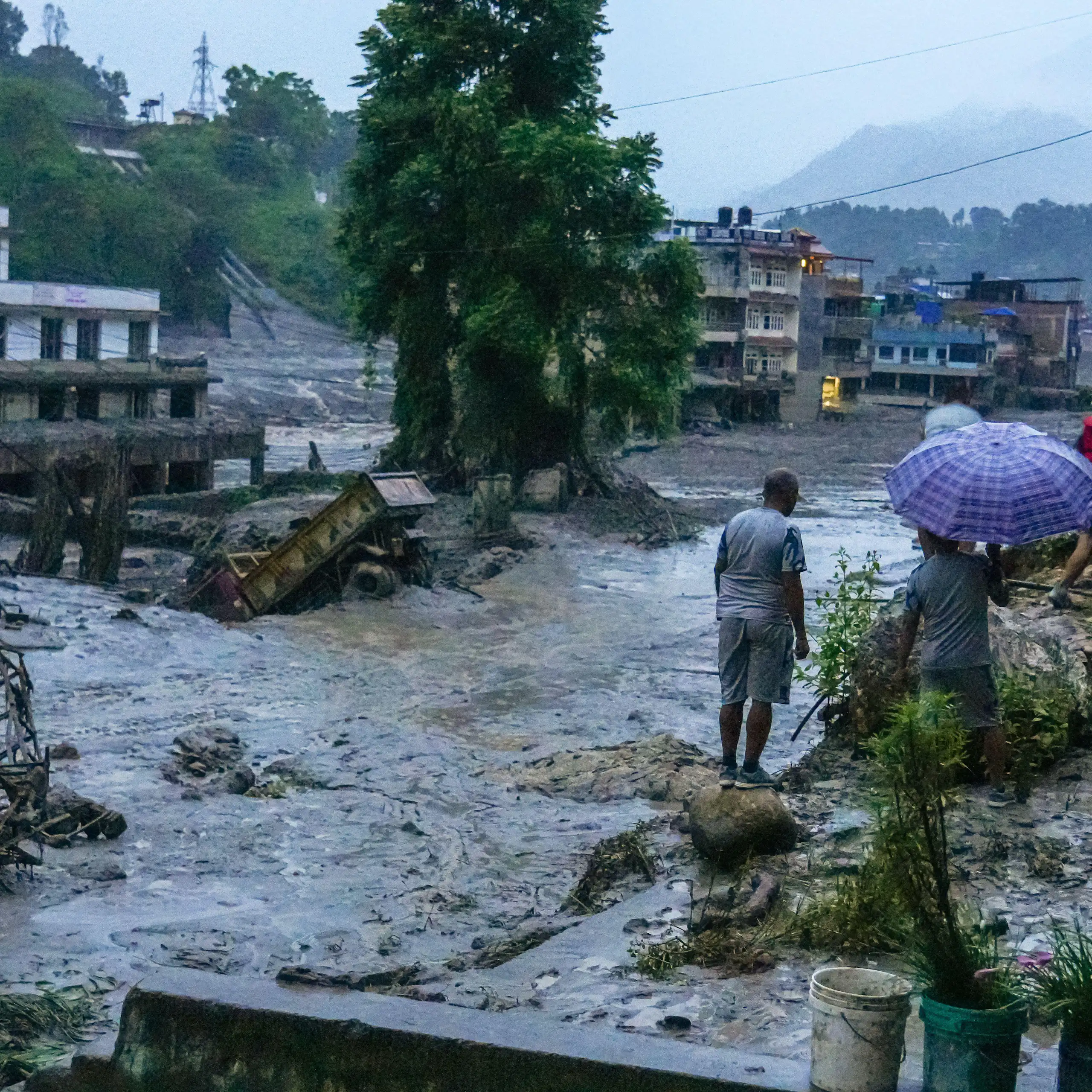 A few people stand at the side of a large area of water caused by the massive flooding in Nepal.