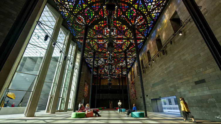 A stained glass ceiling inside a high gallery space, seen from below.
