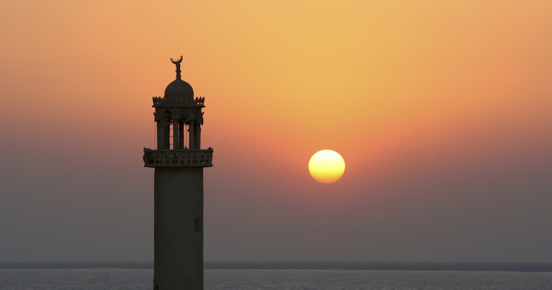 The sun sets behind the minaret of a mosque