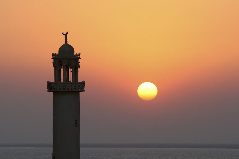 The sun sets behind the minaret of a mosque