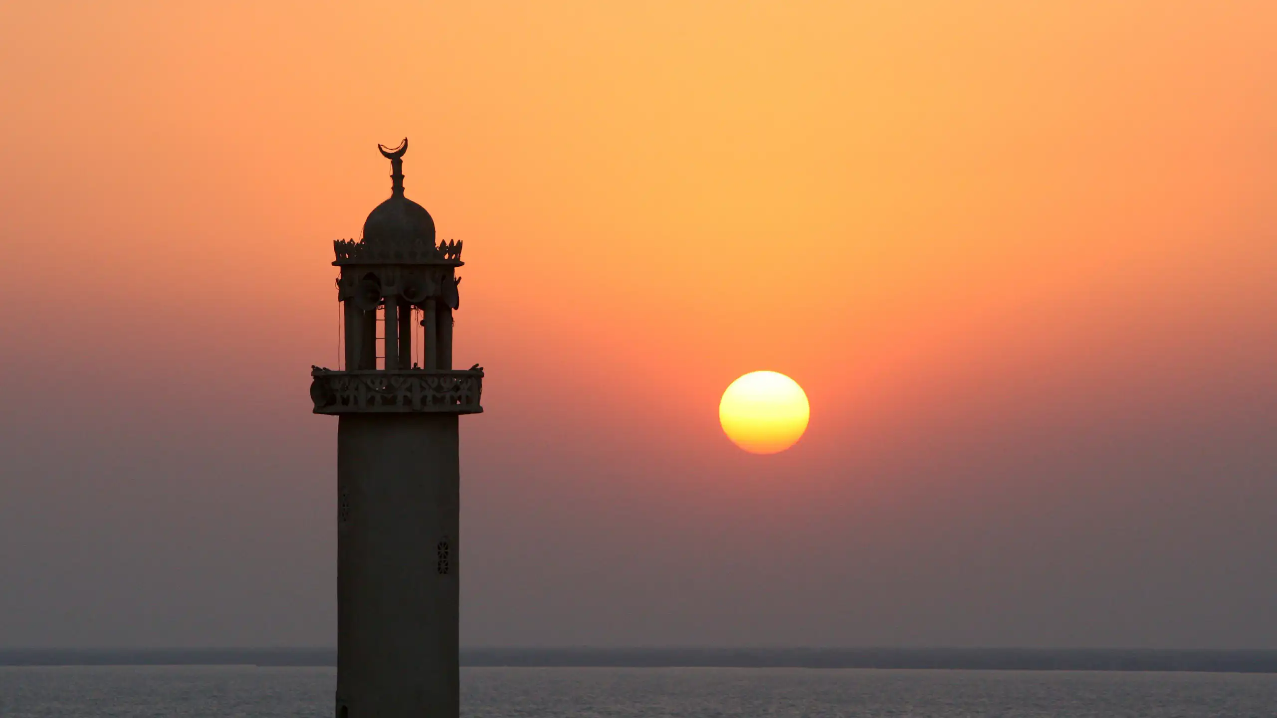 The sun sets behind the minaret of a mosque