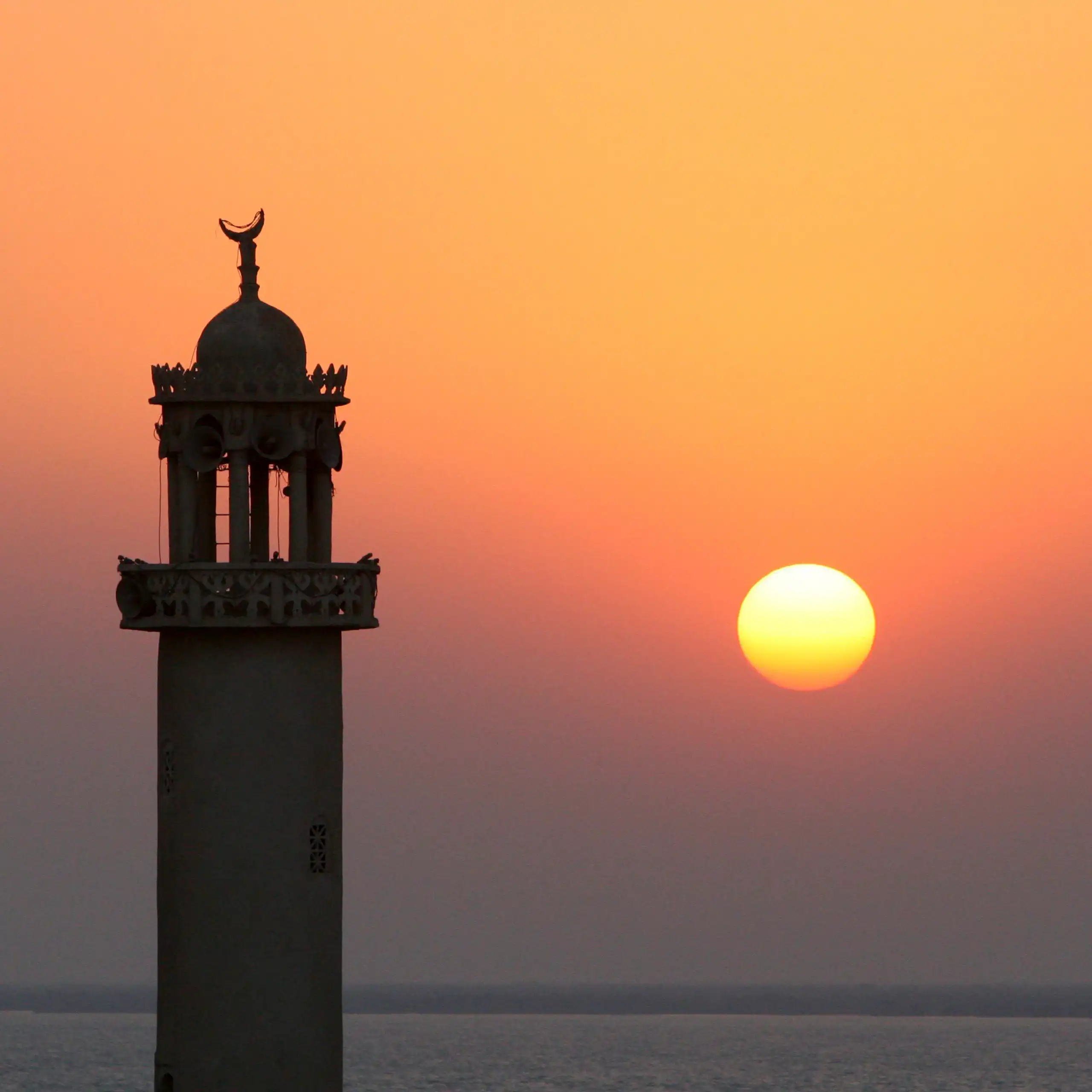 The sun sets behind the minaret of a mosque