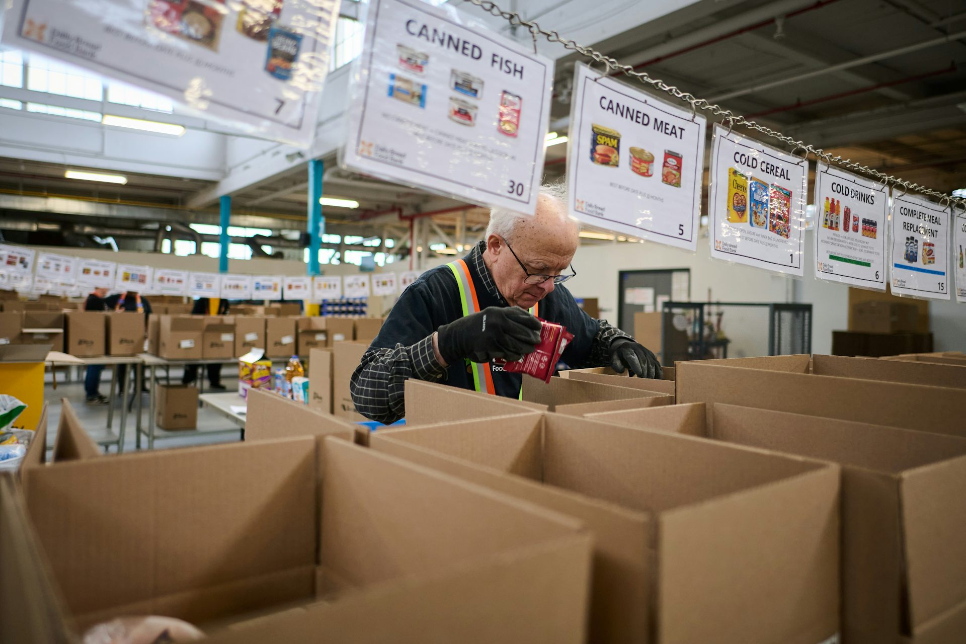A man behind a row of cardboard cartons, with food labels suspended above them