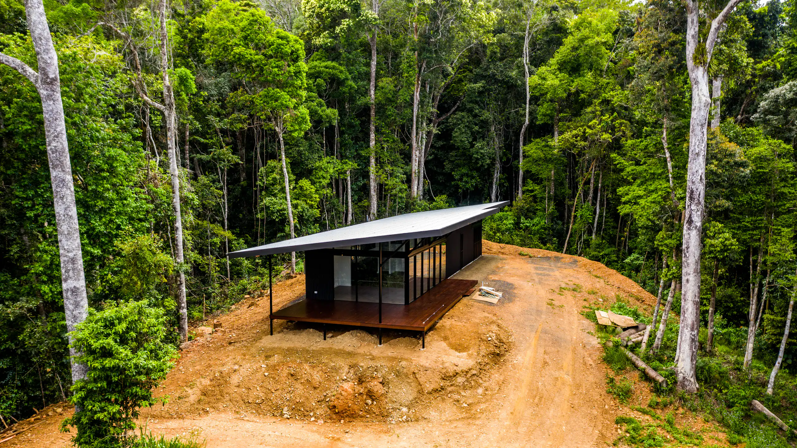 A small, modern house surrounded by lush forest.