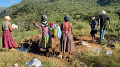 A group of women and one man with small containers, collecting water from a spring in the ground