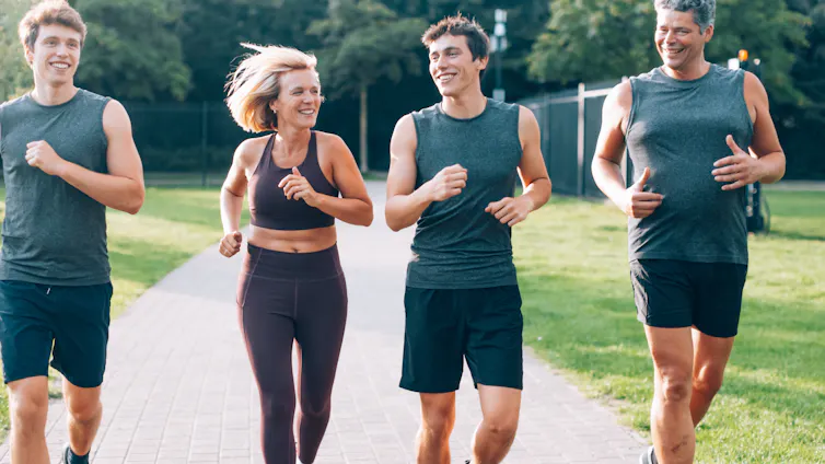 A mother and father jog in a park with their two teenage sons.