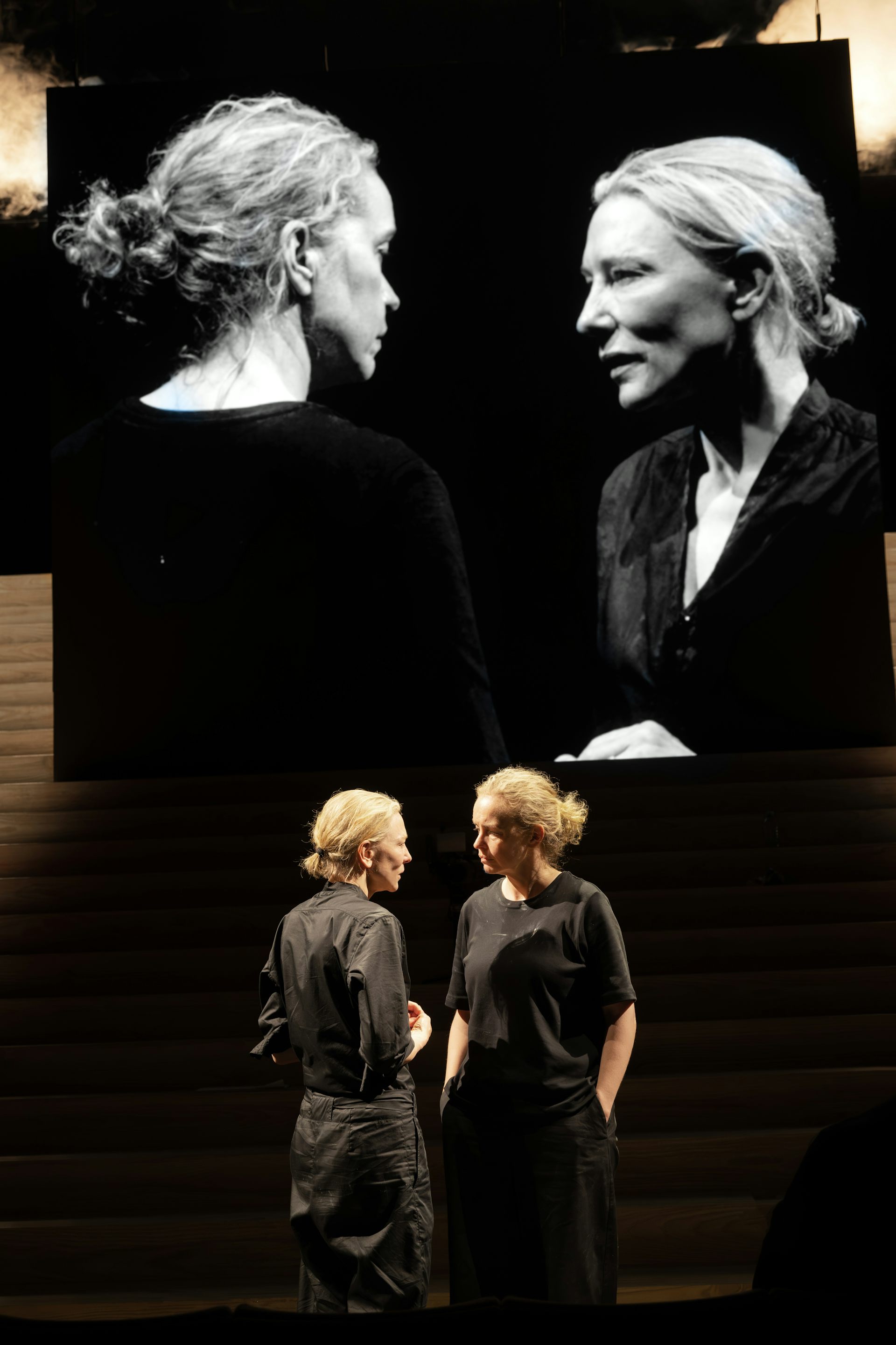 Two women on stage staring at each other, the two projected on screen behind themselves.