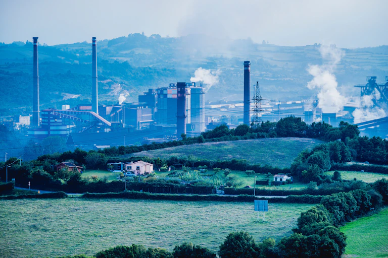Chimeneas de una central térmica emitiendo humo en un paisaje verde de campo con vegetación