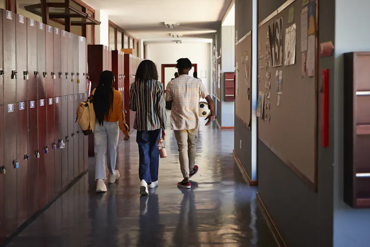 Three young people walk down a school hallway, as seen from behind.