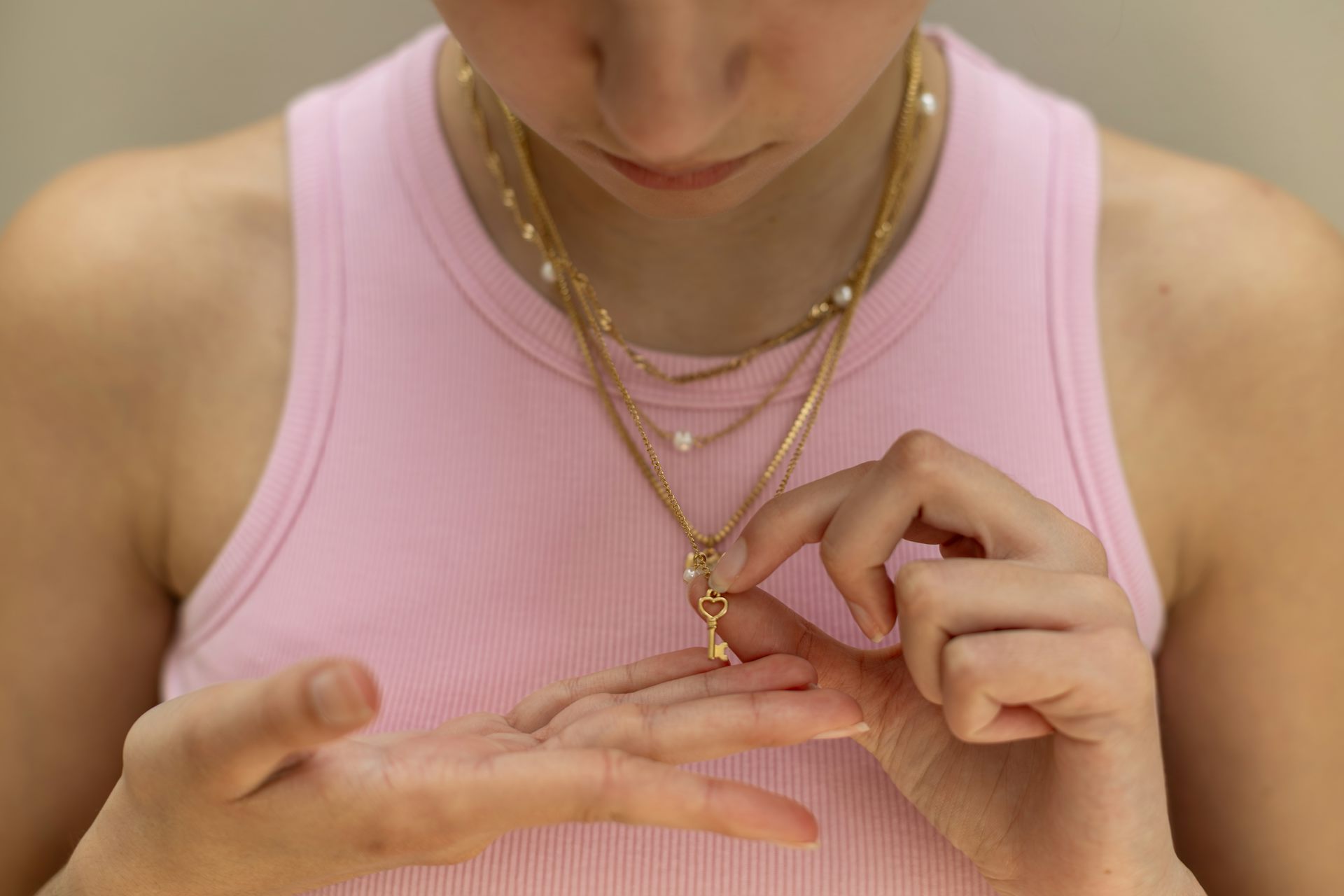 Woman in pink vest top looks down at gold key necklace pendant.