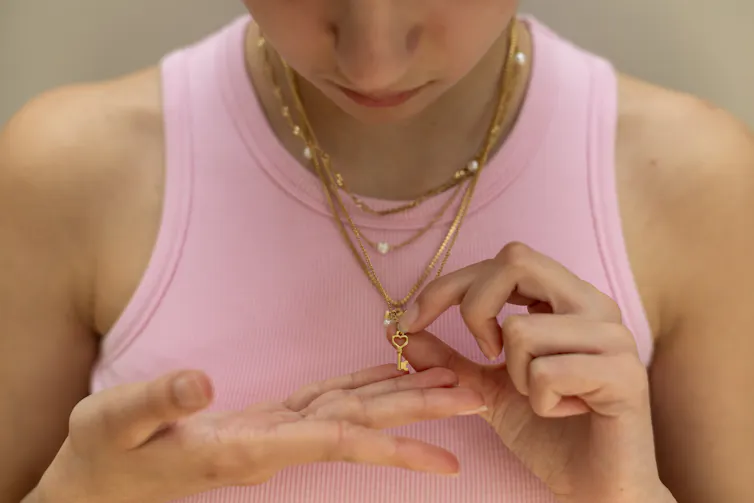Woman in pink vest top looks down at gold key necklace pendant.