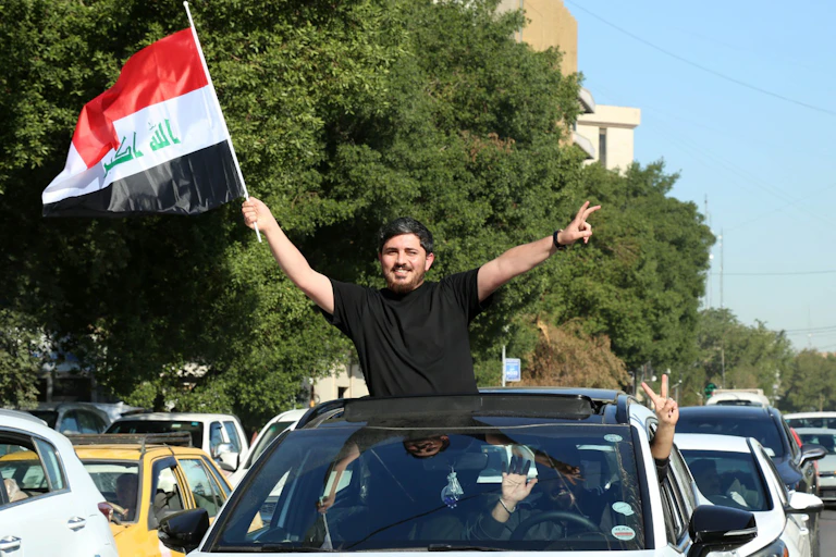 A man waves an Iraqi national flag from the roof of his car.