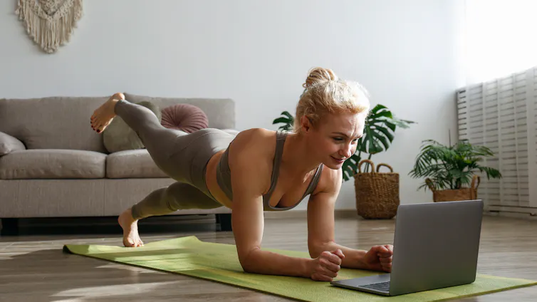 A woman is exercising on the floor of her home whilst looking at a laptop