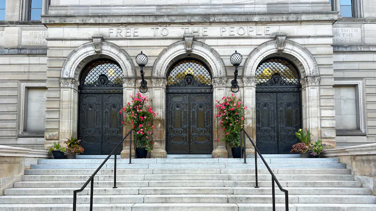 Wide steps with two railings leading up to three arched doorways of Beaux-Arts building