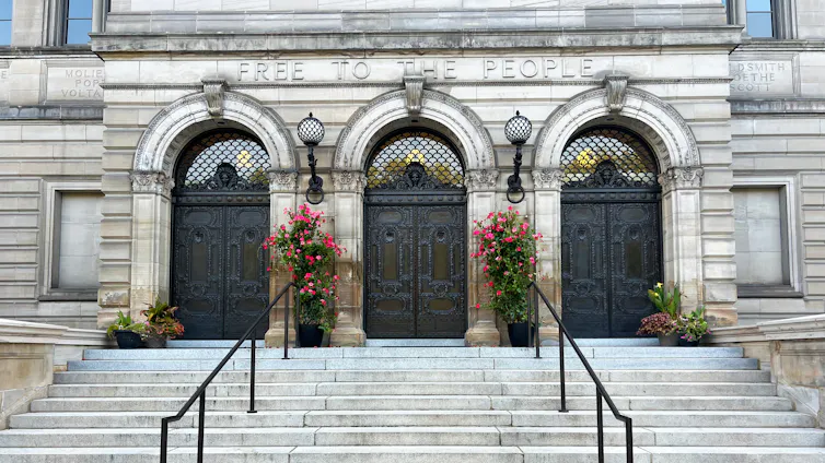 Wide steps with two railings leading up to three arched doorways of Beaux-Arts building