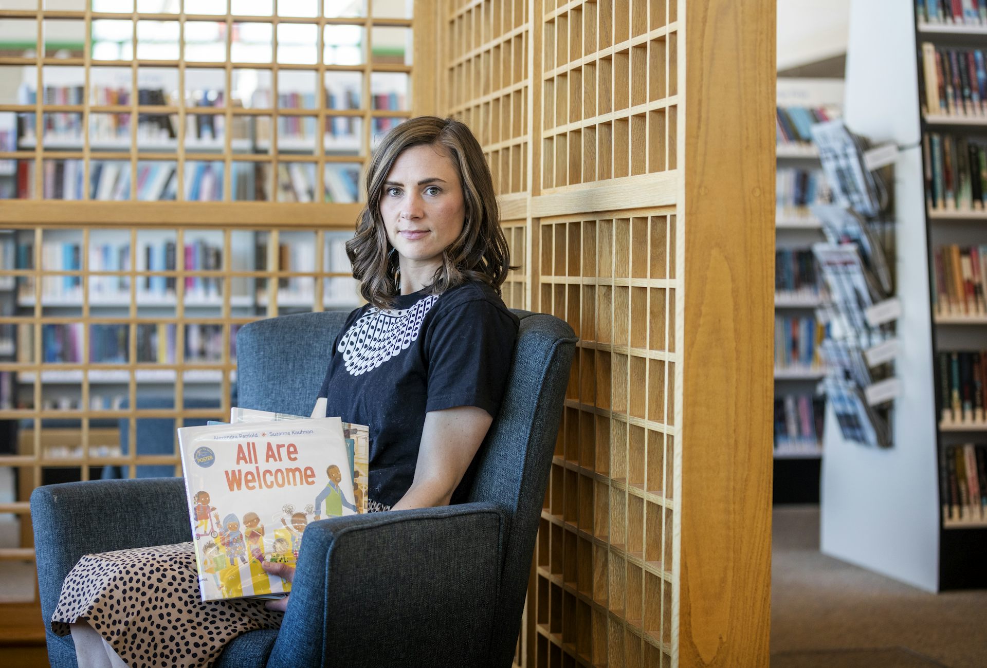 Woman sits in chair holding books in her hand and is surrounded by shelves of books