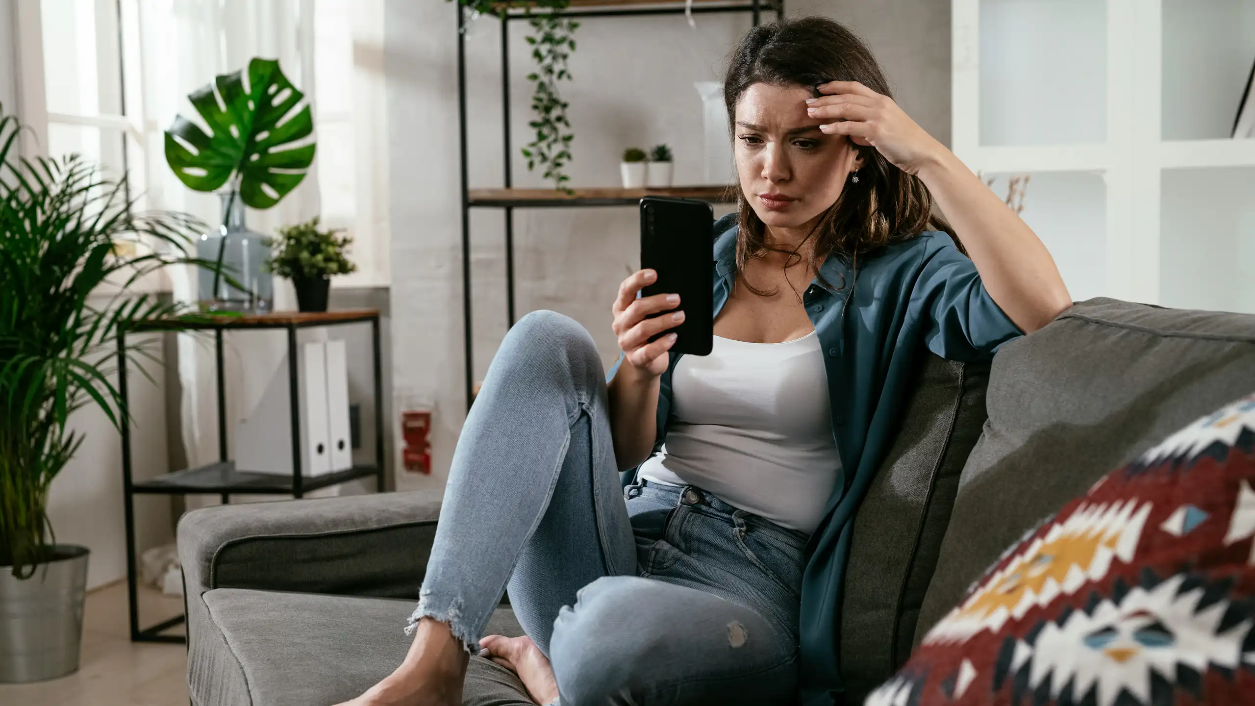 A young woman looks at a callphone while sitting on a couch