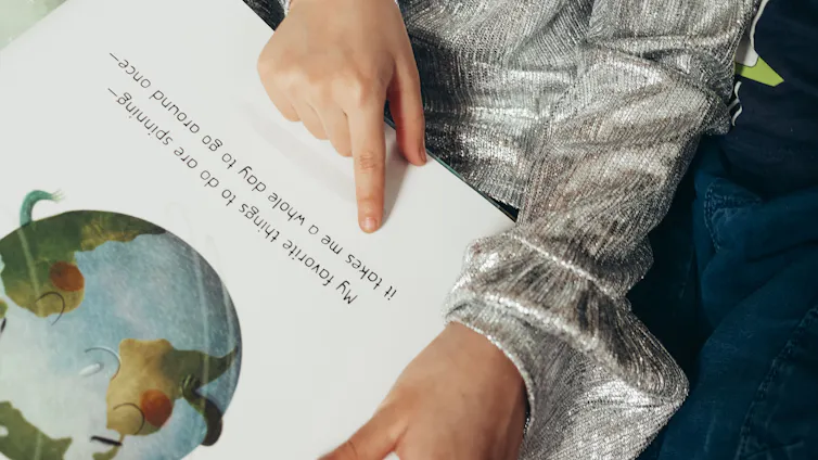 A child places a finger at text on a picture book.