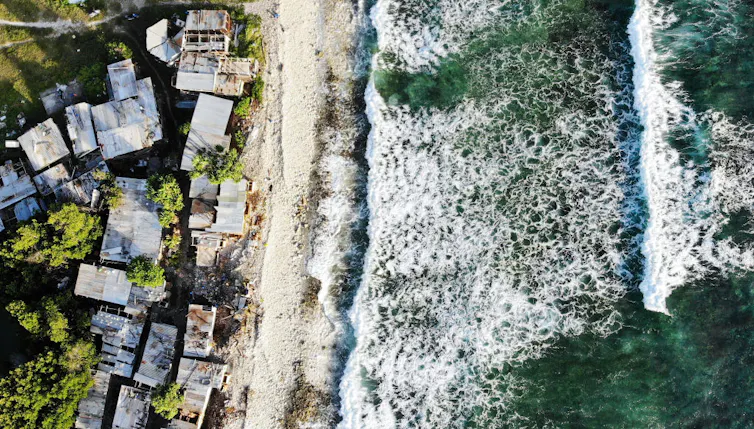 Aerial view of homes in Tuvulu, next to the Pacific Ocean, with ocean waves crashing on the right.