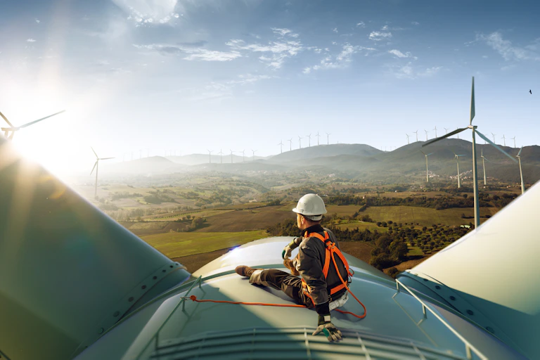 engineer in hi-vis and hard hard sat on top of white wind turbine