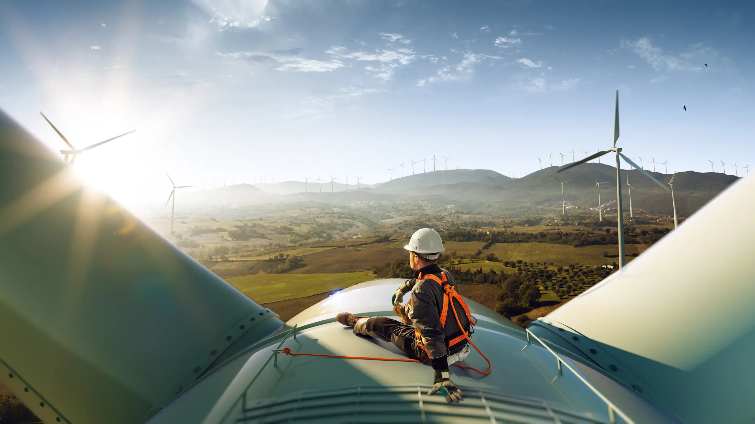 engineer in hi-vis and hard hard sat on top of white wind turbine