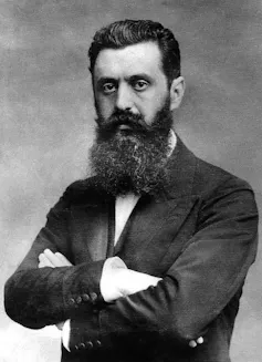 A black and white formal portrait of a bearded man with his arms crossed.