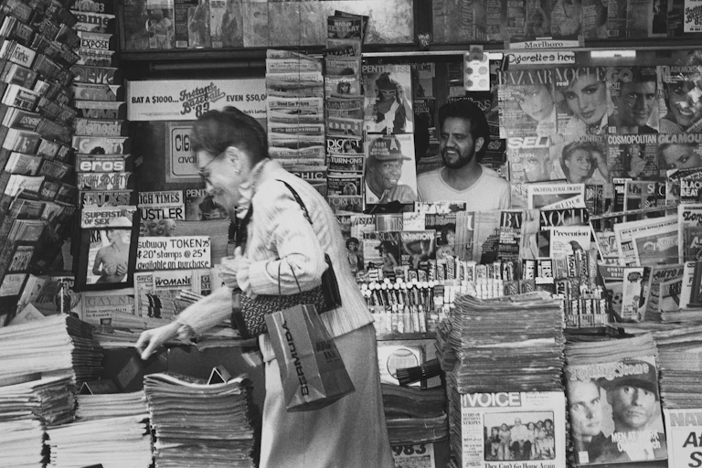 woman reaches for a newspaper in black and white archival photo of a city newsstand