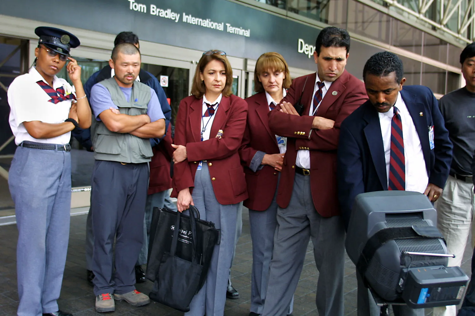 Uniformed people with serious expressions look down at a TV monitor