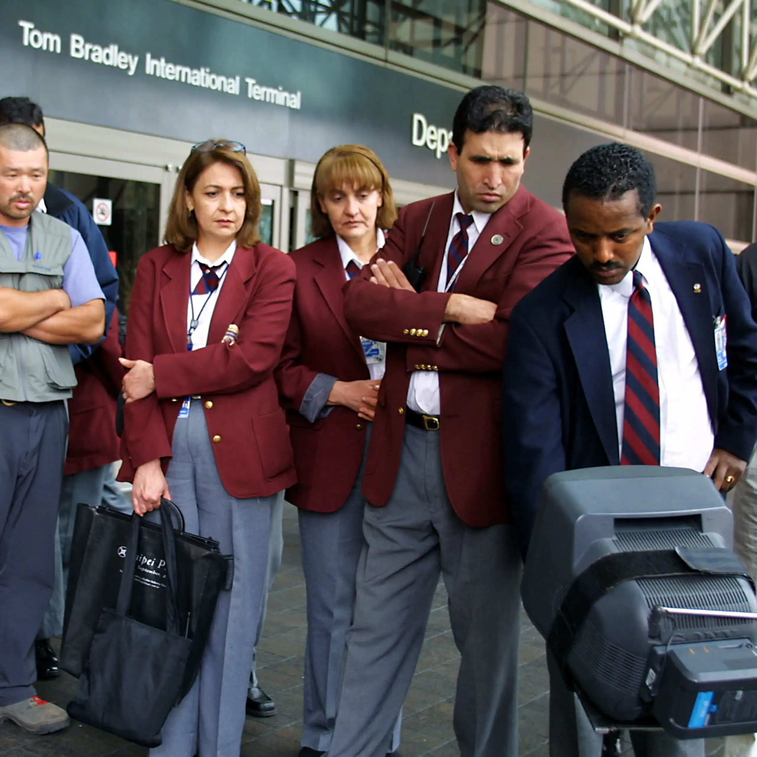 Uniformed people with serious expressions look down at a TV monitor