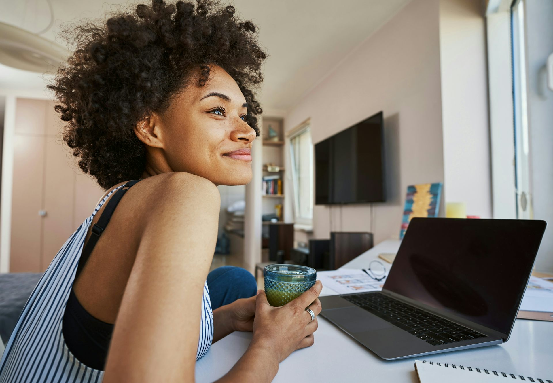 A woman sitting in front of a laptop, looking off to the side with a smile on her face.