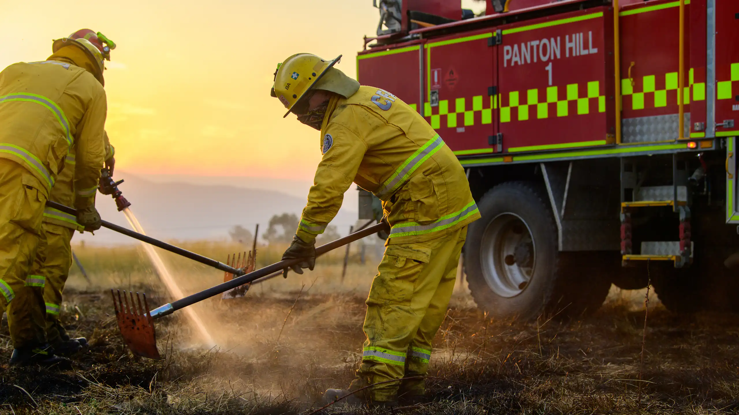 Firefighters put out a grass fire, with a firetruck in the background.