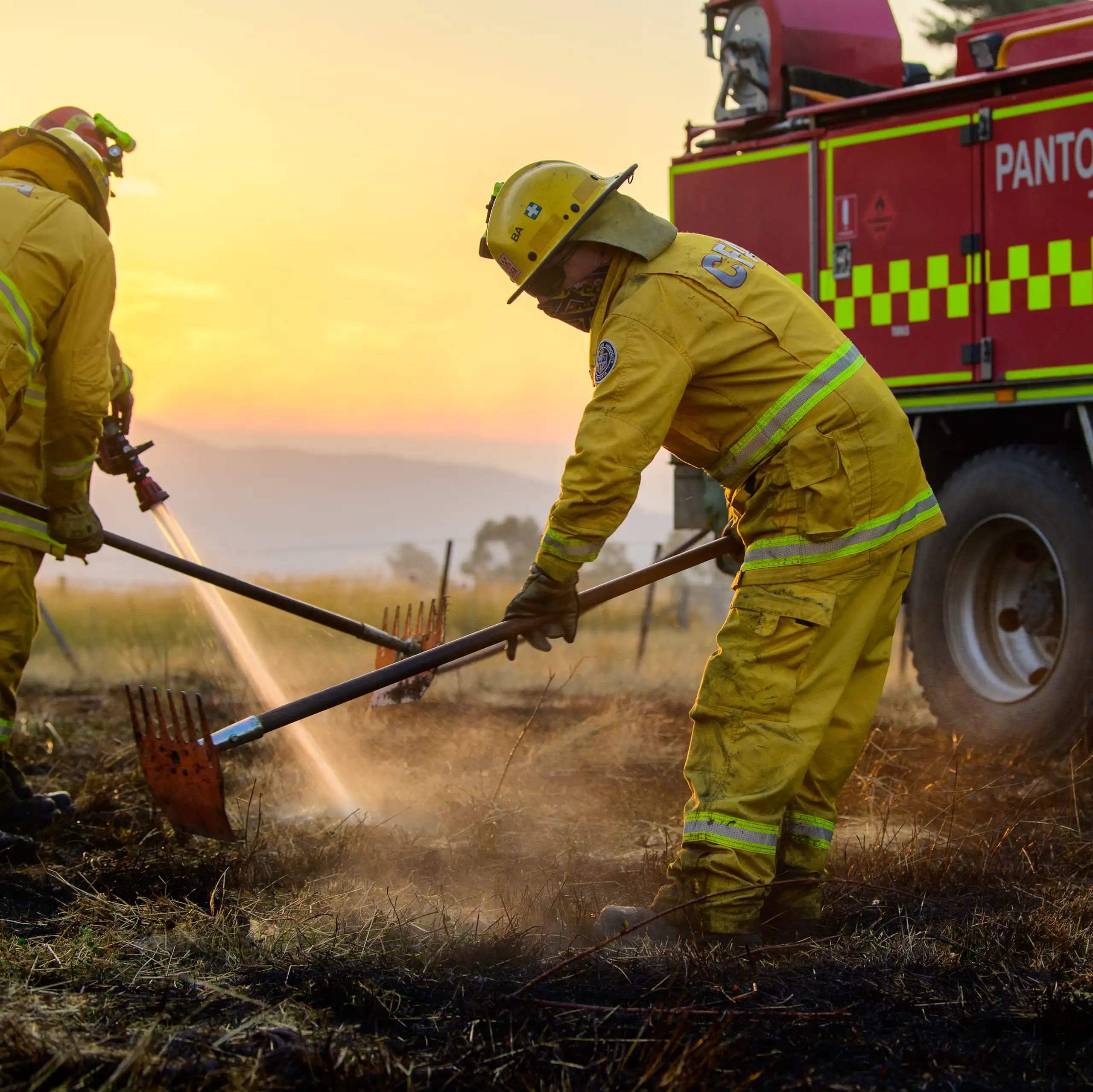 Firefighters put out a grass fire, with a firetruck in the background.