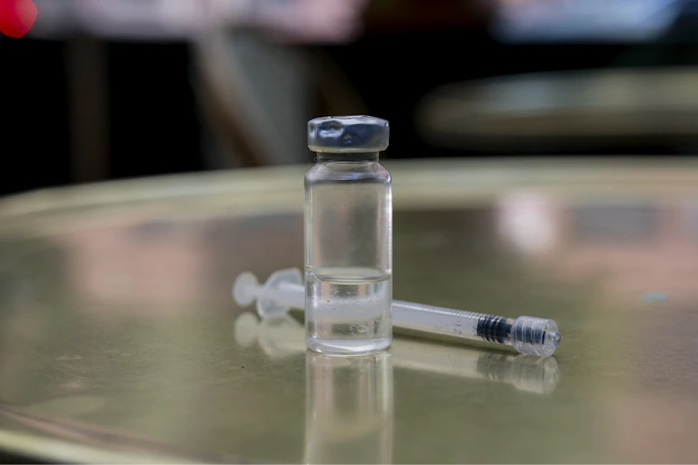 A vial with a clear liquid inside, next to a syringe on a table.