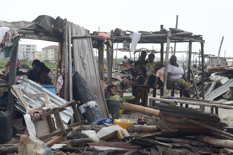 A group of people sitting in the wreckage of a demolished shelter