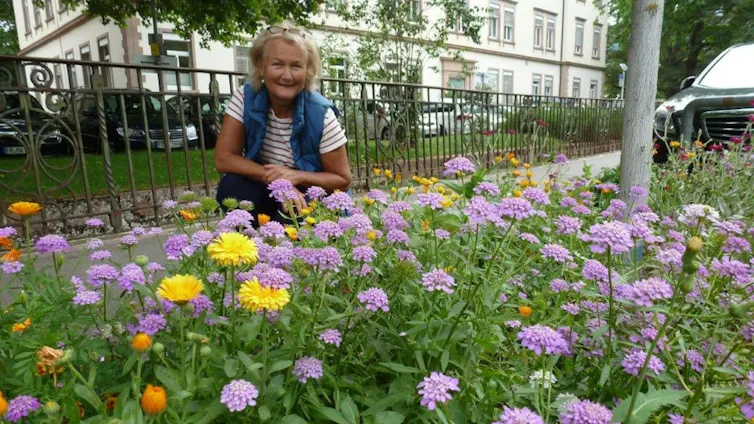 Woman kneels by flowerbeds in city street