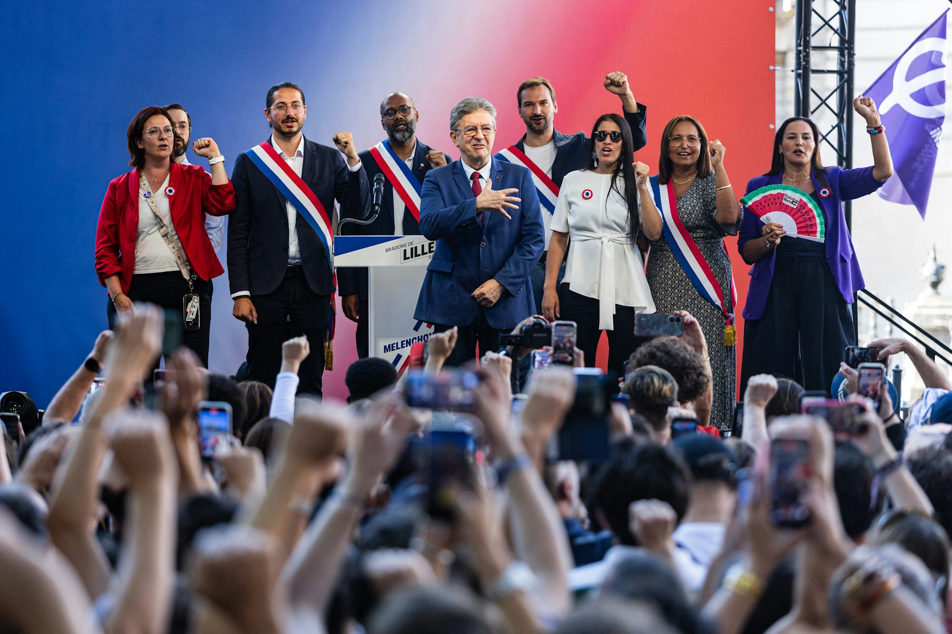 Sur l'estrade, les élus de LFI entourent J.-L. Mélenchon et chantent un hymne.