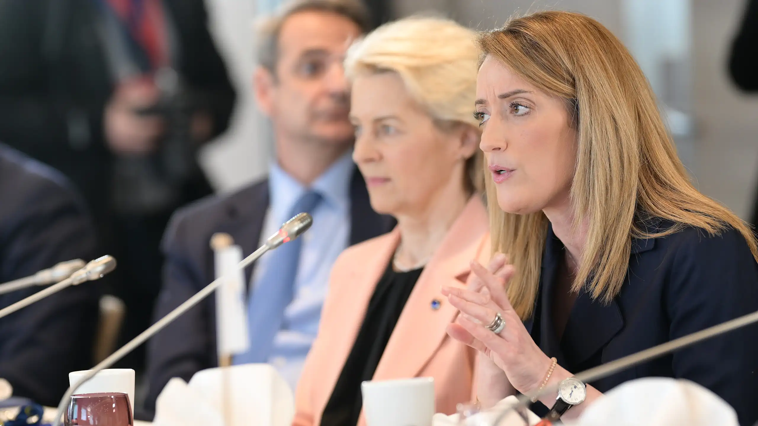 Roberta Metsola speaking into a microphone at a table, with Ursula von der Leyen sitting to her right