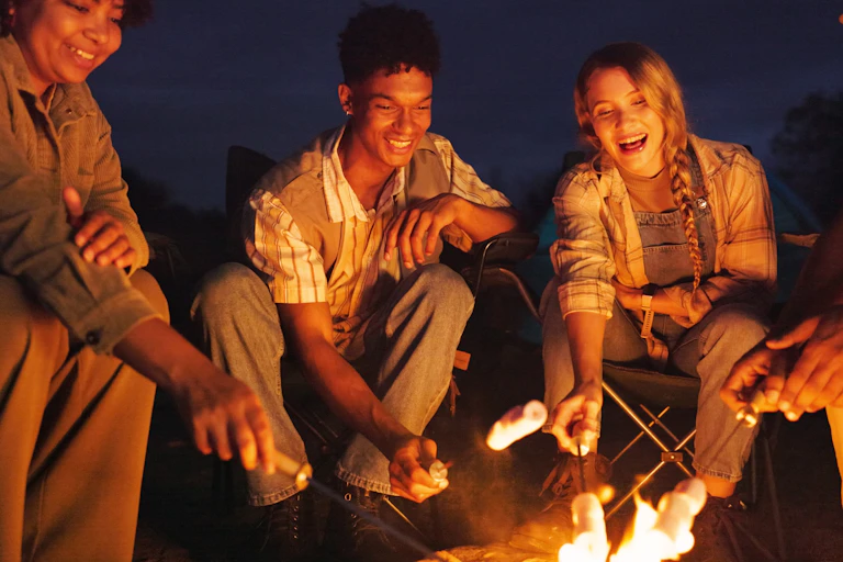 Group of adults gathered around a campfire roasting marshmellows