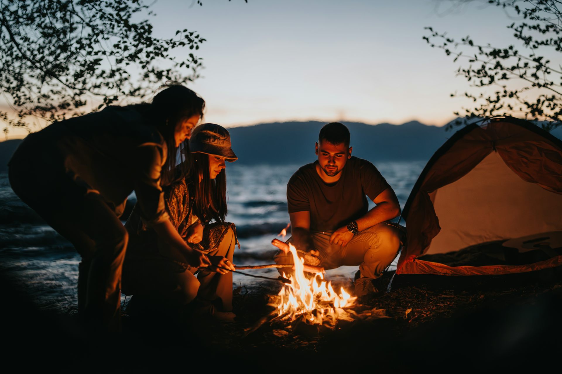 Three adults tend to a campfire