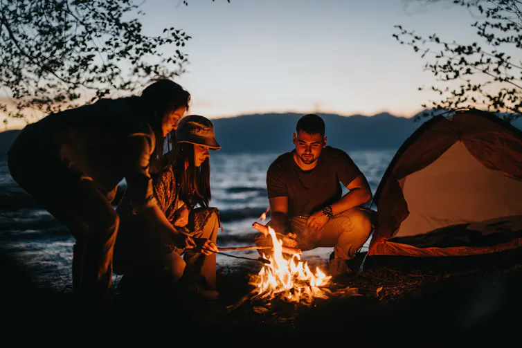 Three adults tend to a campfire