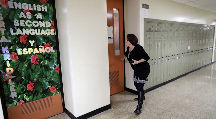 A woman stands near a closed wooden door in an empty school hallway.