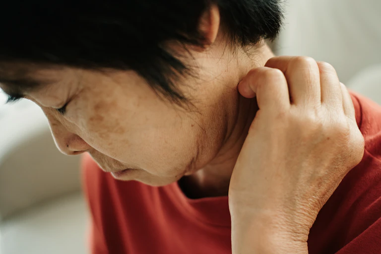 Person looking down with eyes closed, scratching at a rash on the back of their neck